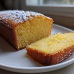 Close-up of a loaf of moist olive oil cake, sliced, showing a tender crumb and lemon zest.