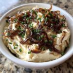 A close-up of creamy homemade onion dip topped with crispy caramelized onions and fresh chives.