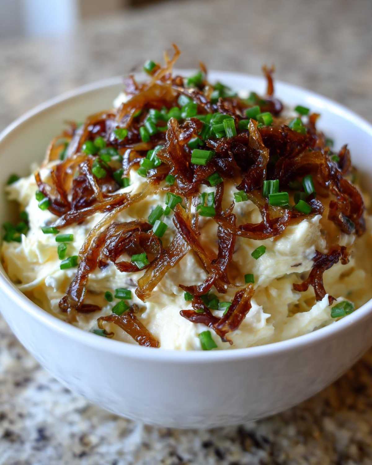 Close-up of a creamy onion dip topped generously with crispy fried onions and fresh chopped chives.