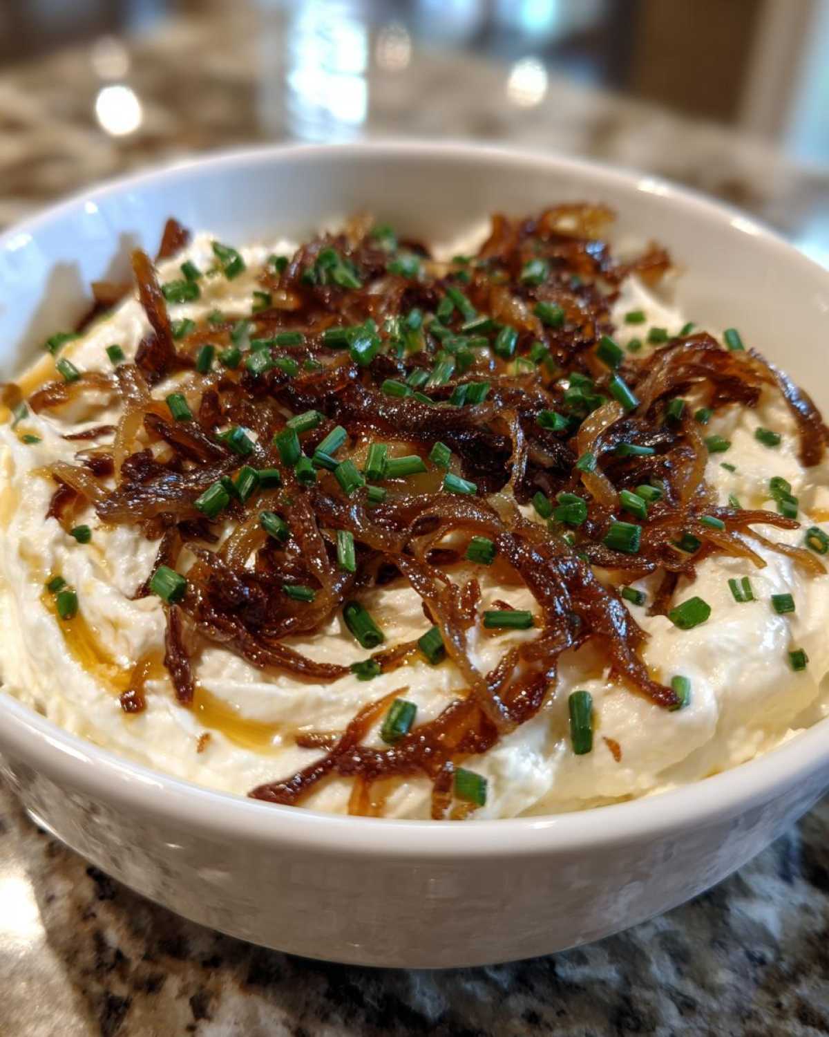 Close-up of creamy homemade onion dip topped generously with caramelized crispy onions and fresh chives.