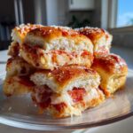A stack of cheesy pepperoni pizza sliders with golden brown tops sprinkled with Parmesan cheese.