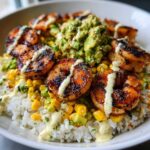 Close-up of a delicious shrimp bowl featuring grilled shrimp, white rice, corn, avocado mash, and a creamy drizzle.