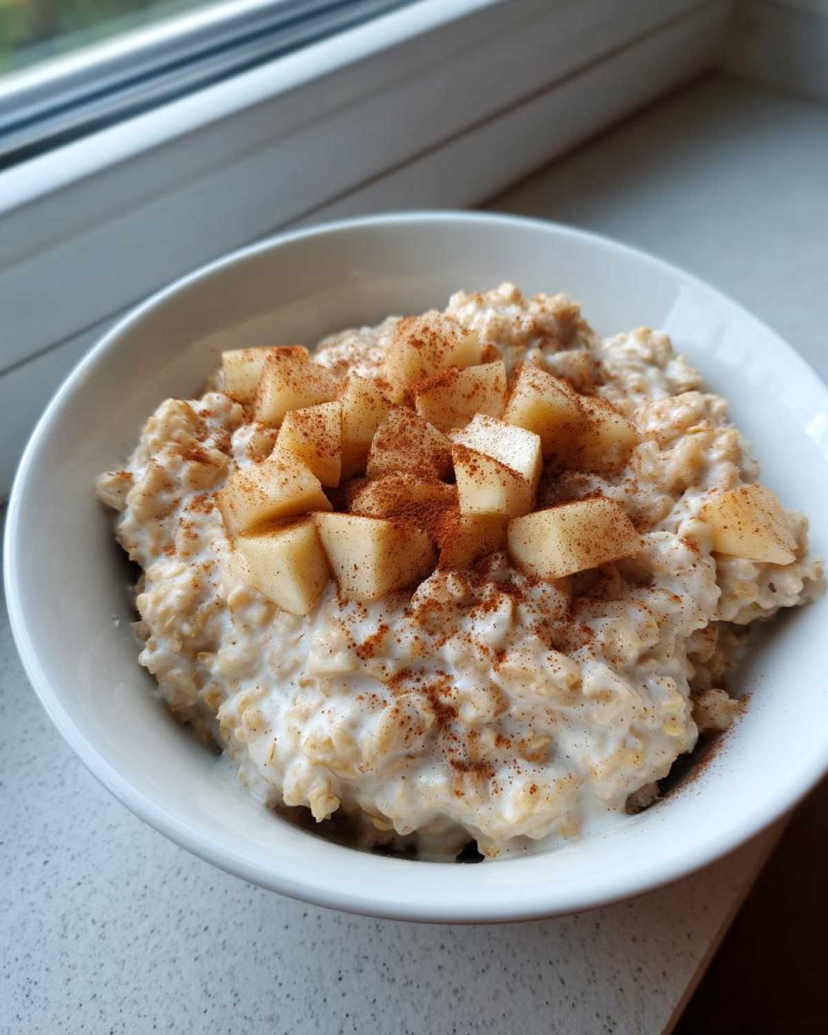Close-up of creamy apple cinnamon oatmeal topped with diced apples and a generous sprinkle of cinnamon.