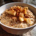 Close-up of a white bowl filled with creamy apple cinnamon oatmeal, topped with diced apples and sprinkled cinnamon.