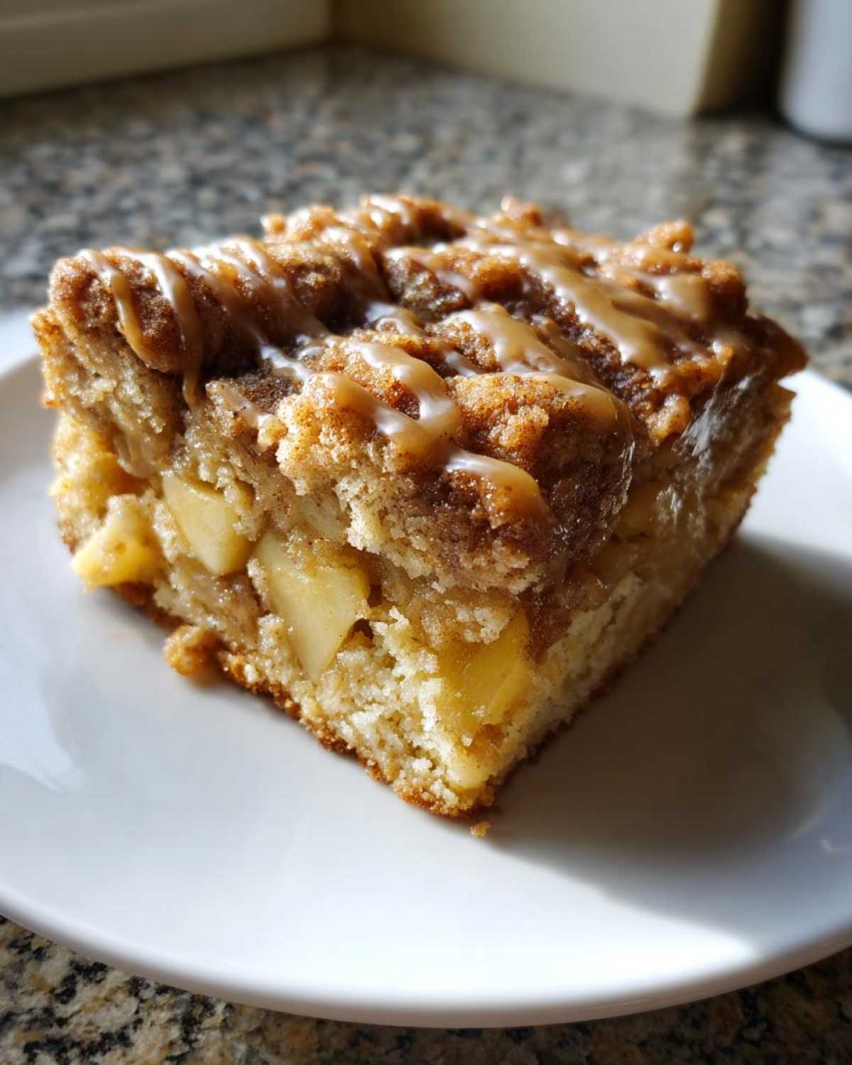 Close-up of a moist slice of apple crumb cake topped with cinnamon streusel and a caramel glaze.