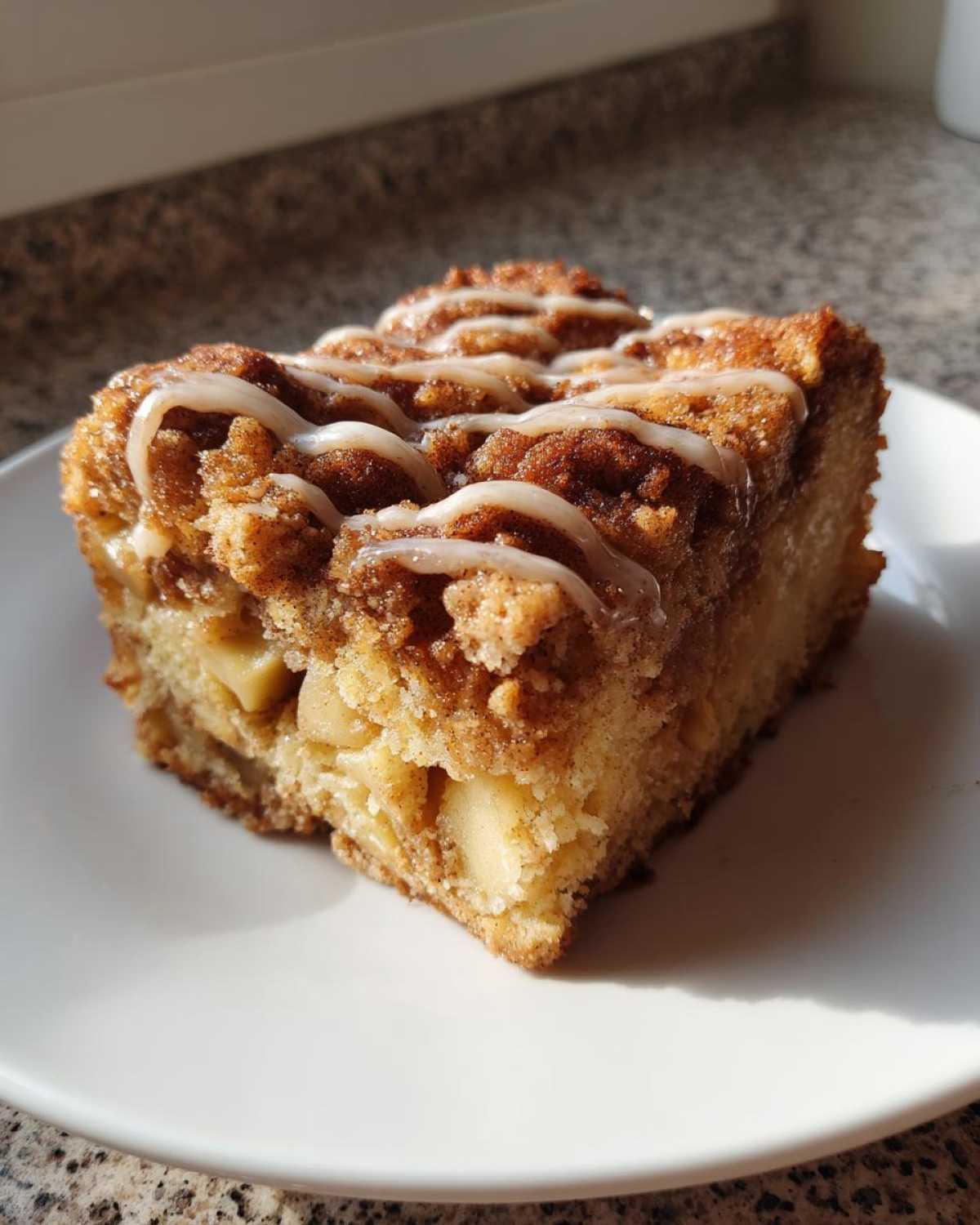Close-up of a moist slice of apple crumb cake topped with cinnamon streusel and a white vanilla glaze drizzle.