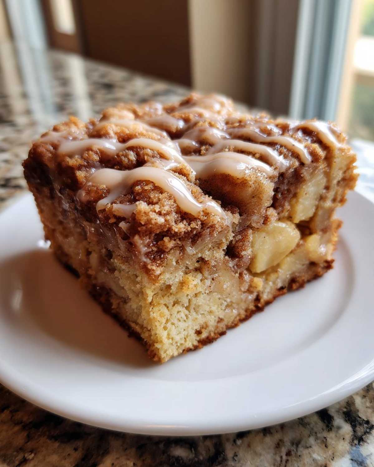 Close-up of a moist slice of apple crumb cake topped with cinnamon streusel and a vanilla glaze.
