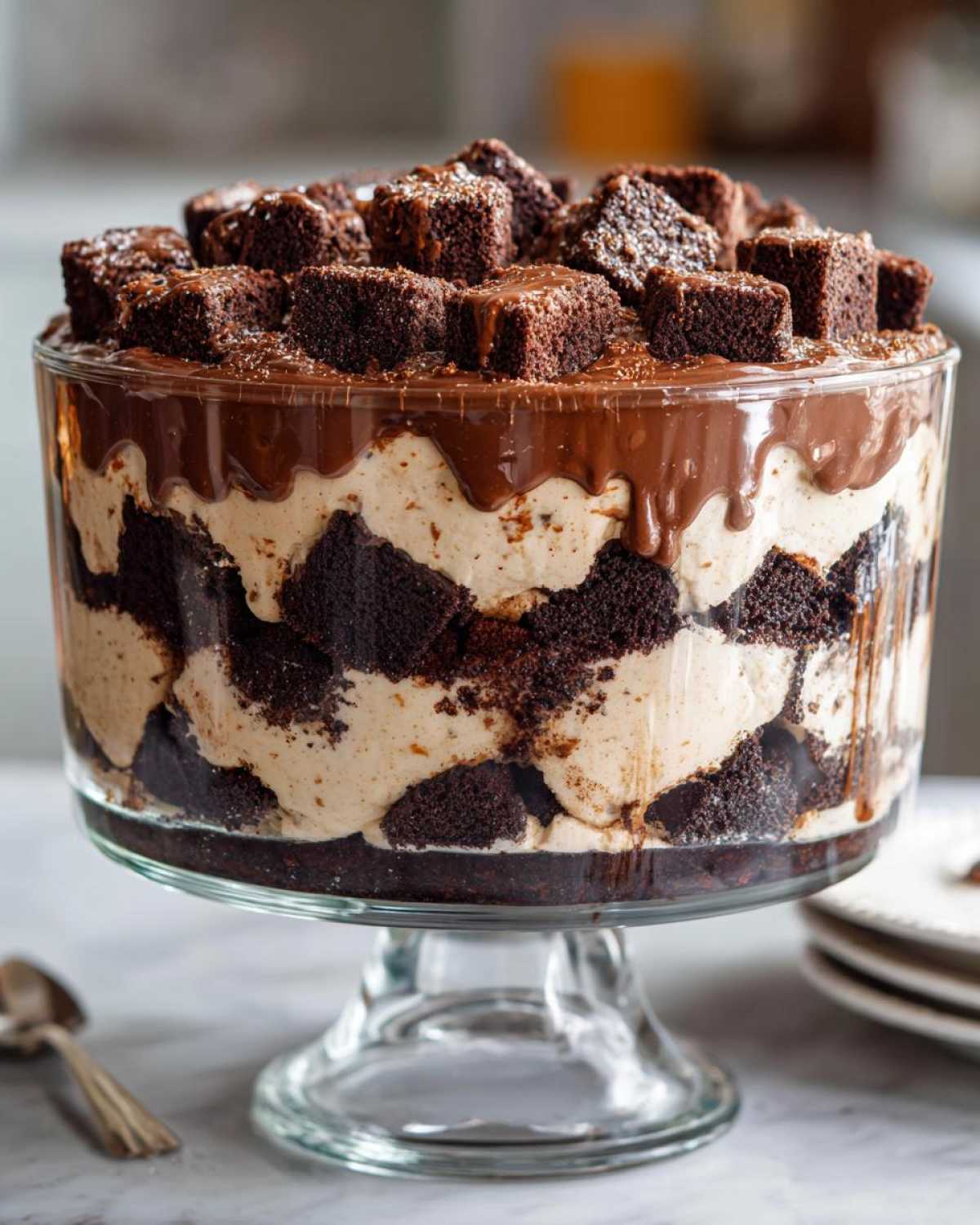 A multi-layered Baileys Chocolate Cheesecake Trifle featuring dark cake pieces and light cream filling, topped with chocolate ganache and brownie cubes.