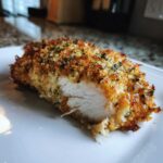 Close-up of a juicy baked ranch chicken breast, showing the white interior and crispy, herbed crust.