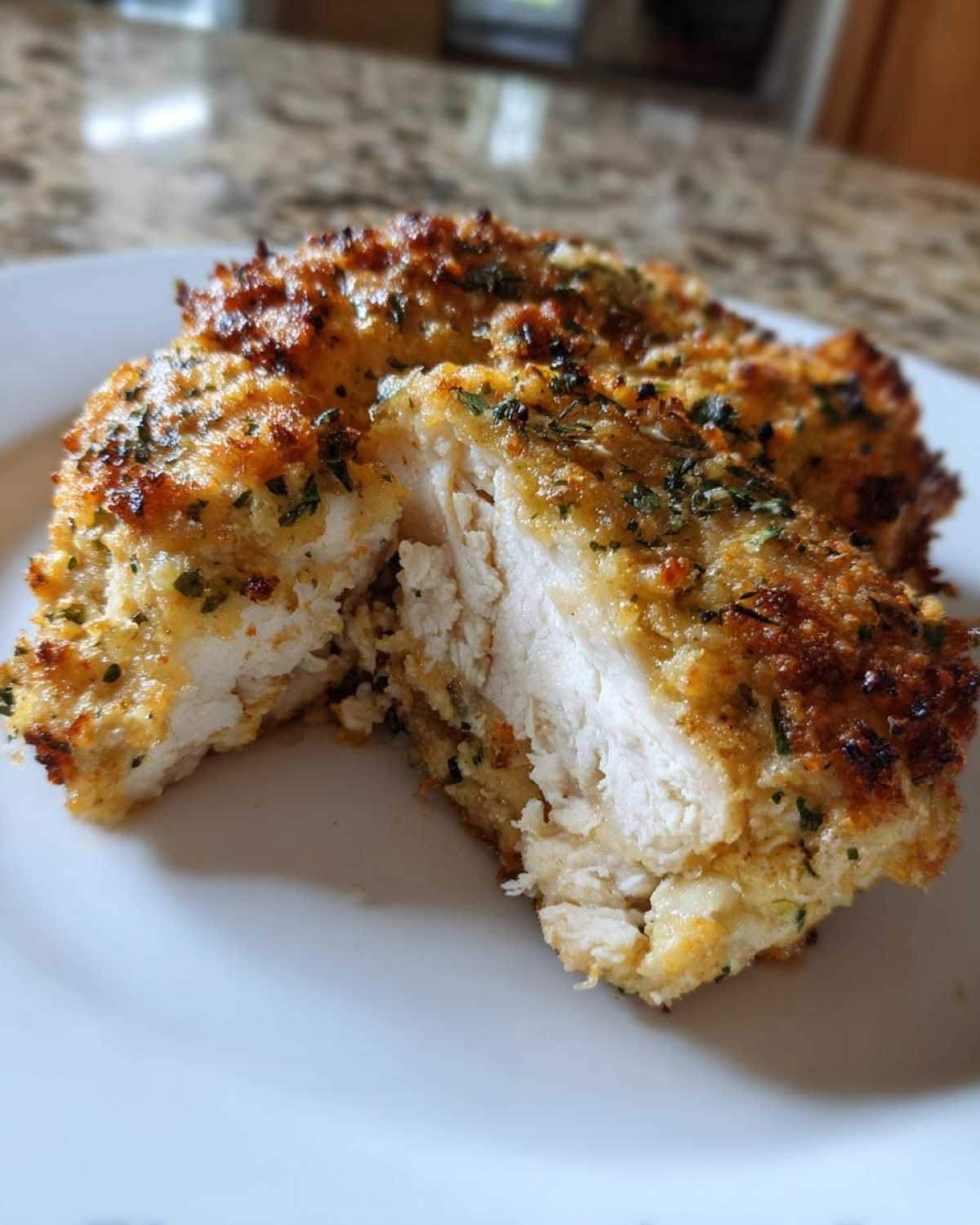 Close-up of baked ranch chicken cut in half, showing the juicy white interior and crispy, seasoned crust.