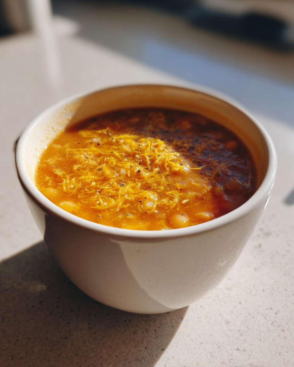 A close-up of a white bowl filled with savory chickpea soup, topped with melted shredded orange cheese and pepper.