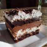 A decadent slice of brownie refrigerator cake showing layers of dark cake, chocolate mousse, and whipped cream.
