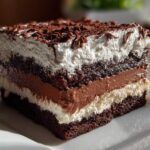 Close-up of a rich, layered brownie refrigerator cake slice topped with whipped cream and chocolate shavings.