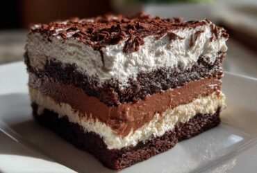 Close-up of a rich, layered brownie refrigerator cake slice topped with whipped cream and chocolate shavings.
