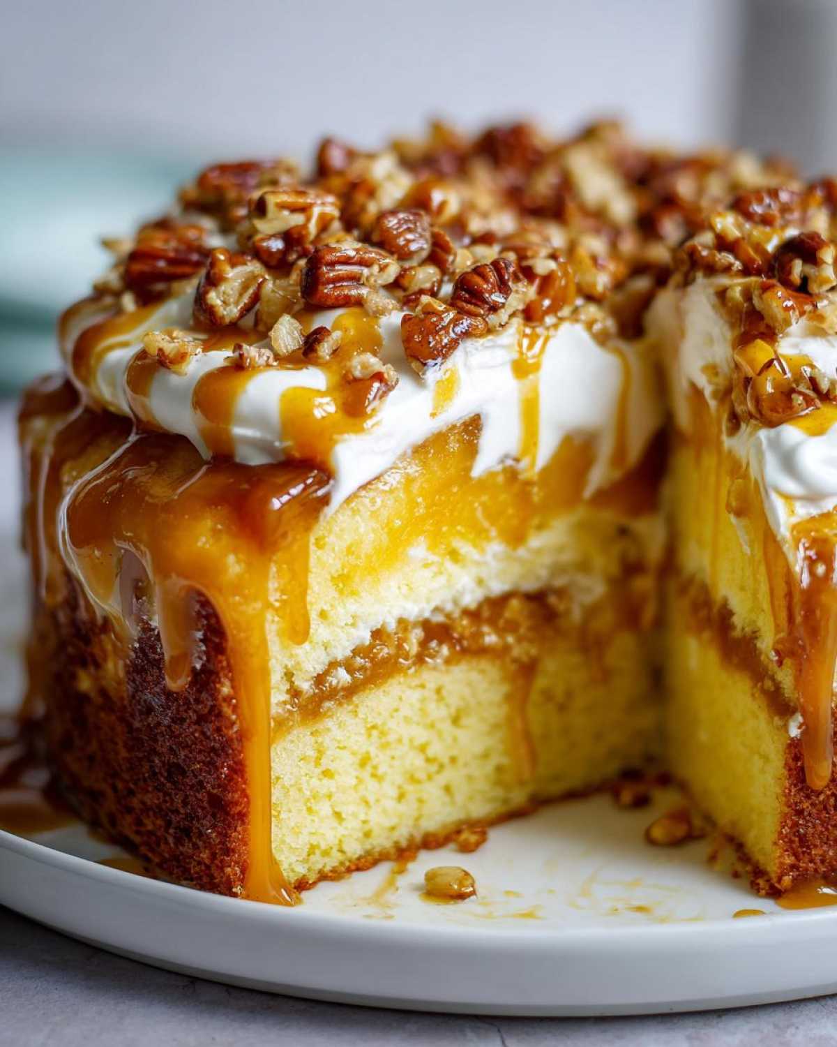 A slice cut from a moist butter pecan praline poke cake, topped with whipped cream, caramel sauce, and chopped pecans.