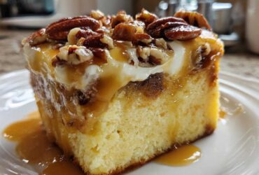 A close-up of a slice of moist butter pecan praline poke cake topped with whipped cream, caramel sauce, and pecans.