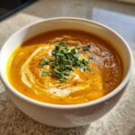A close-up of rich, orange butternut squash soup topped with a swirl of cream and fresh parsley.