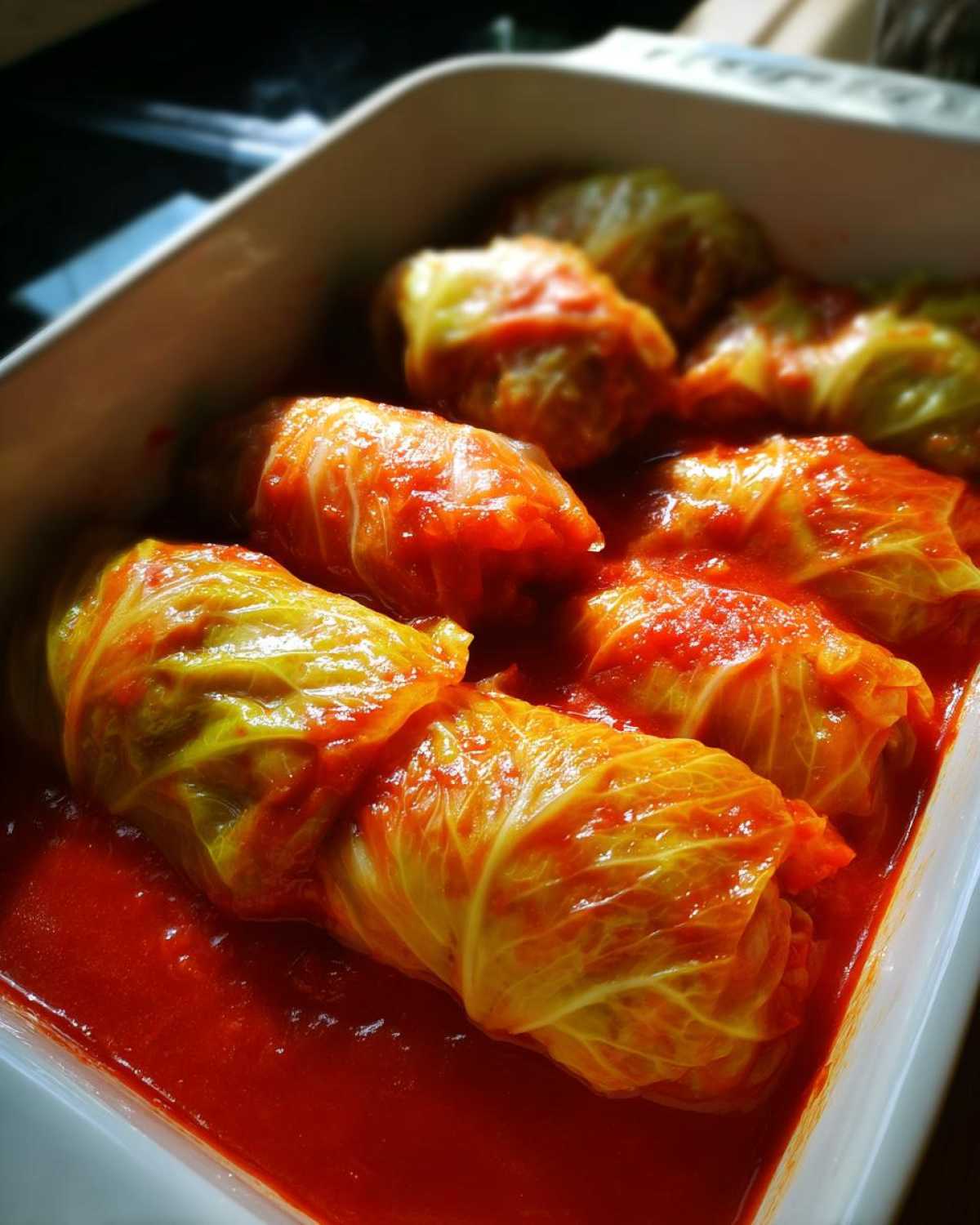 Close-up of several homemade cabbage rolls simmering in a bright red tomato sauce in a white baking dish.