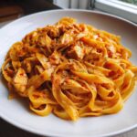 Close-up of a white plate piled high with creamy cajun chicken pasta featuring fettuccine noodles and seasoned chicken chunks.