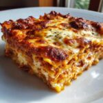 Close-up of a square slice of baked ravioli casserole with bubbly, browned cheese topping.
