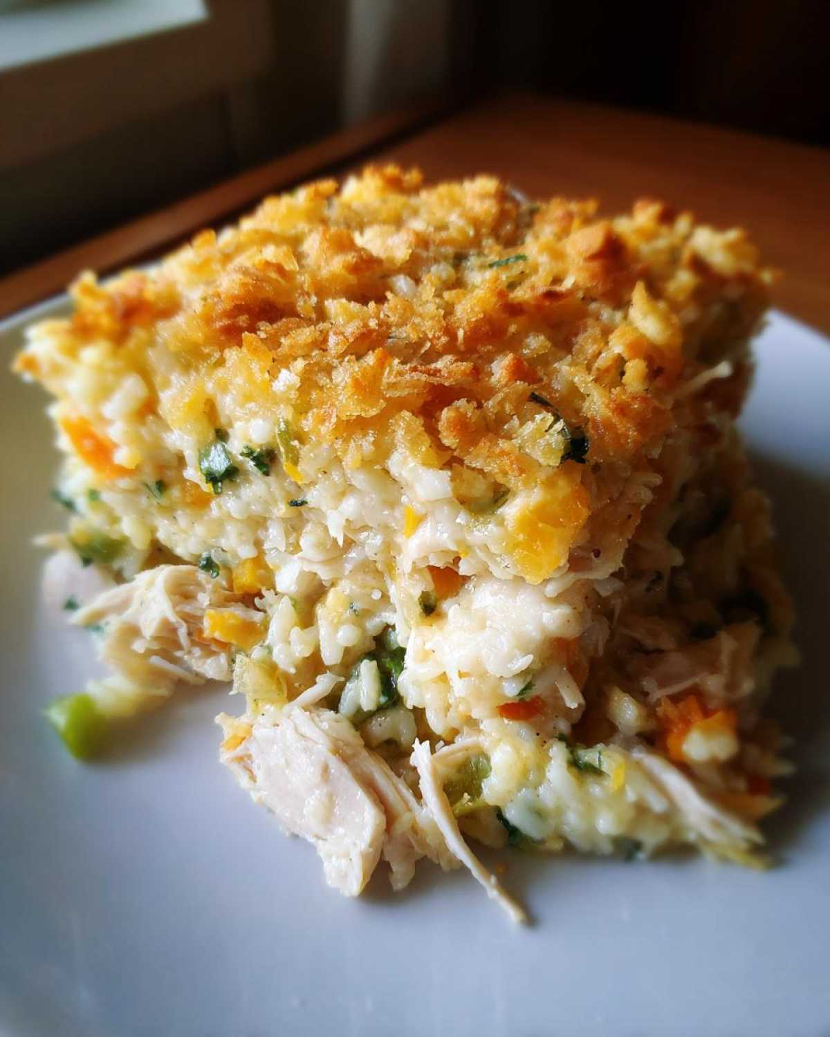 A close-up of a square serving of cheesy rice casserole with shredded chicken and vegetables, topped with crispy breadcrumbs.