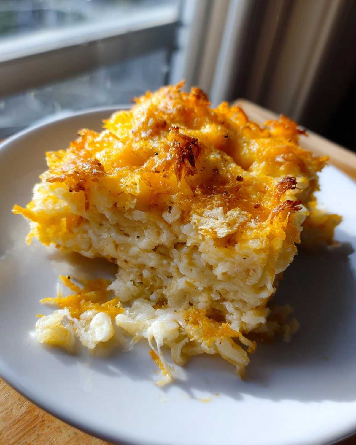 A close-up serving of cheesy potato casserole showing shredded potatoes and a golden, crispy cheesy topping.
