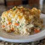 A hearty serving of cheesy rice casserole featuring shredded chicken, peas, carrots, and a golden, crunchy breadcrumb topping.