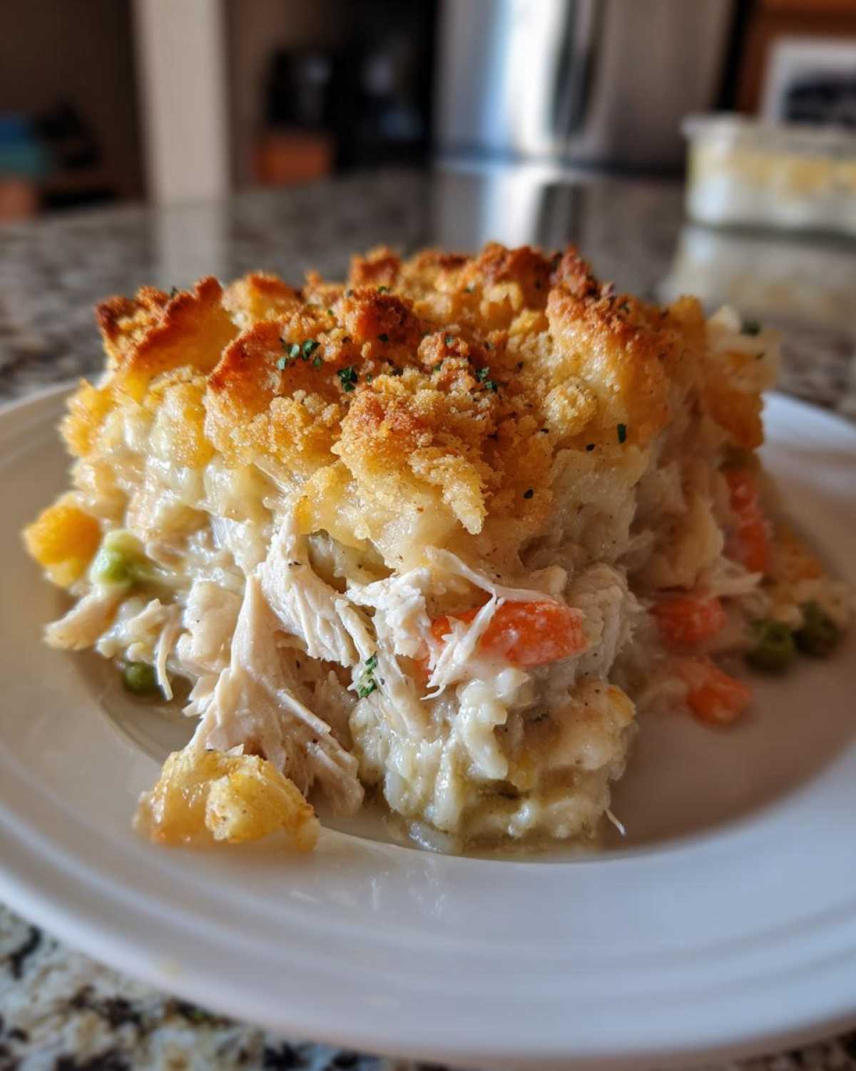 A close-up serving of creamy chicken and rice casserole with visible shredded chicken, carrots, peas, and a golden, crispy topping.