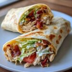 A close-up of a delicious chicken bacon ranch wrap, cut in half to show shredded chicken, bacon, lettuce, and ranch dressing.