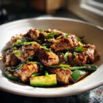 Close-up of glossy chicken zucchini stir fry pieces coated in dark sauce, garnished with green onions.