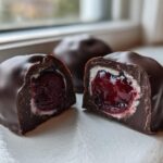 Close-up of a chocolate covered cherries cut in half, showing the dark chocolate shell, white fondant layer, and juicy cherry center.