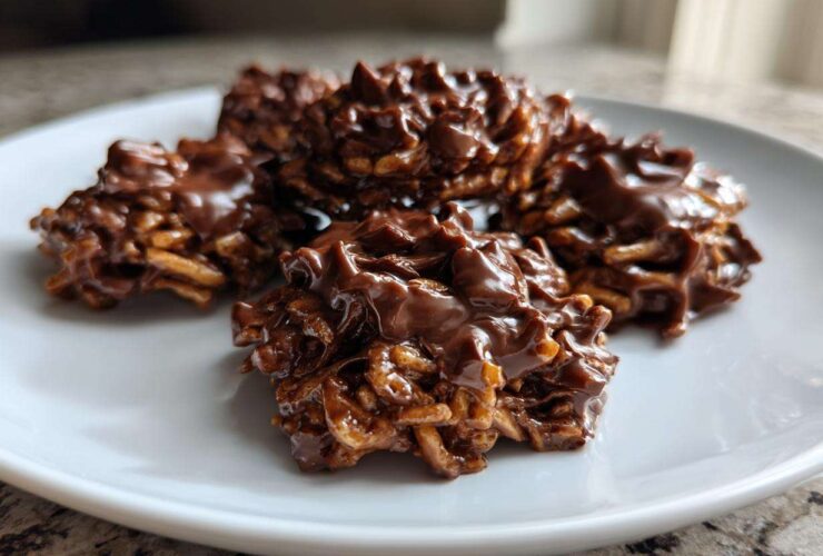 A close-up shot of several glossy, chocolate-covered haystack cookies piled on a white plate.