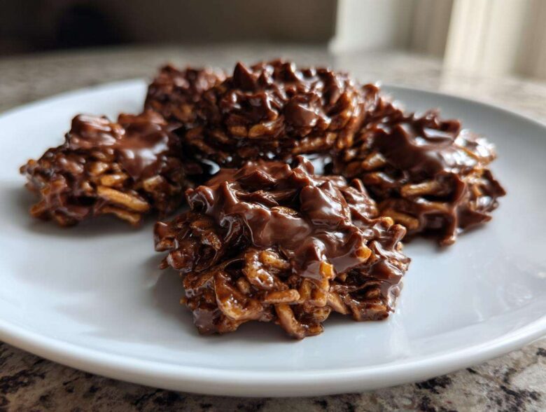 A close-up shot of several glossy, chocolate-covered haystack cookies piled on a white plate.