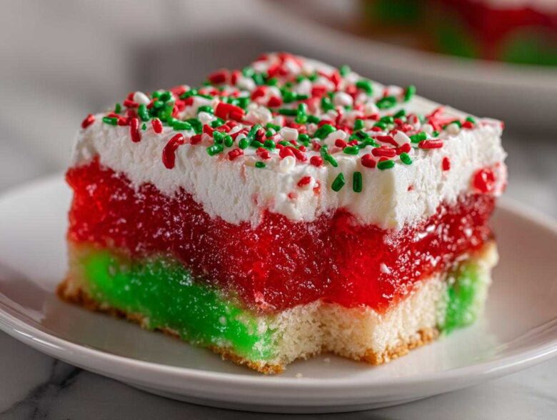 Close-up of a slice of Christmas poke cake featuring layers of green and red jello, white whipped topping, and holiday sprinkles.