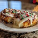 Two delicious christmas tree cinnamon rolls covered in white icing and red and green holiday sprinkles.