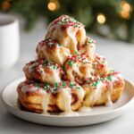 A stack of warm christmas tree cinnamon rolls drizzled with white icing and covered in red and green sprinkles.