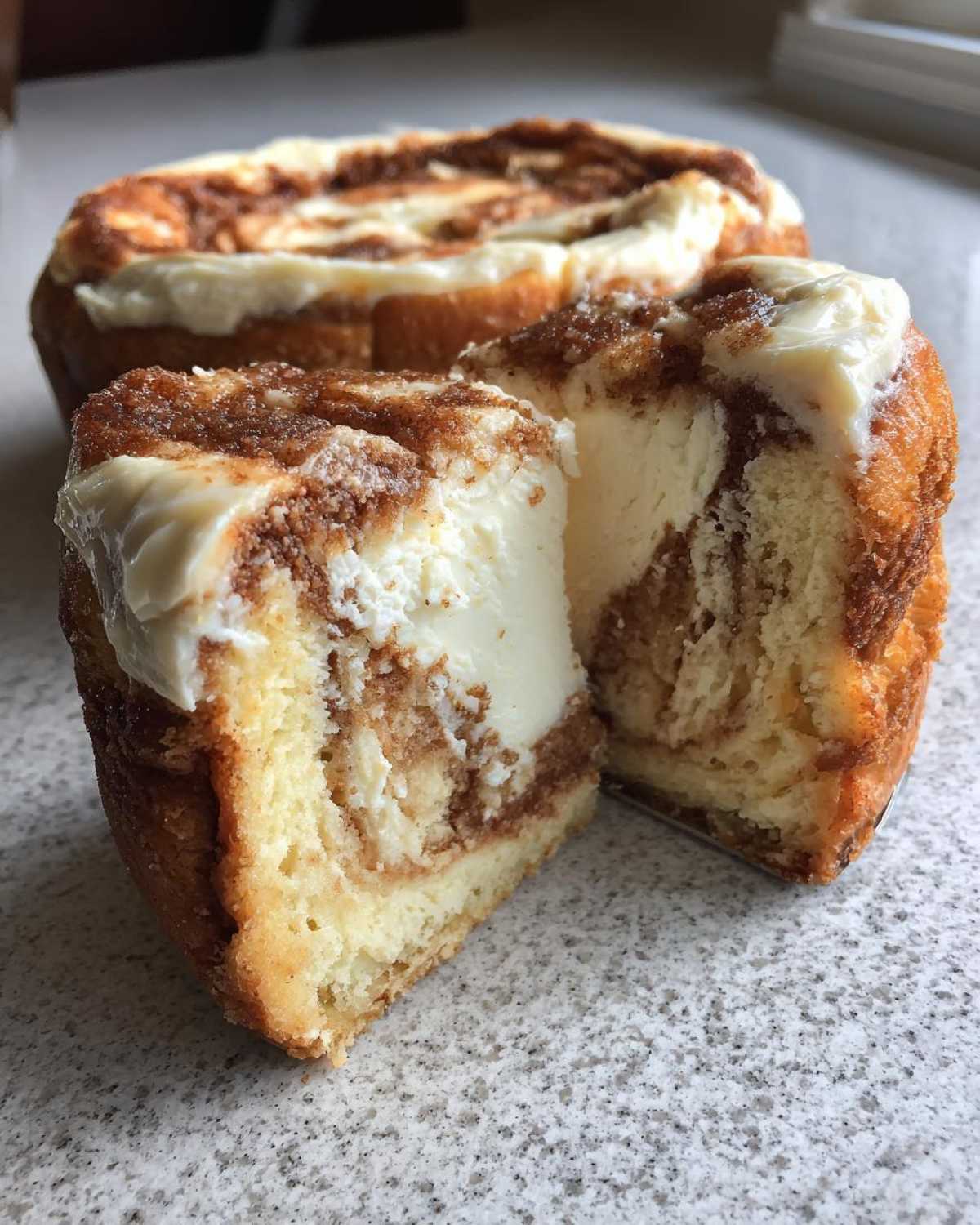 A close-up view of a cinnamon roll cheesecake cut in half, showing the creamy filling and cinnamon swirl.