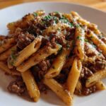 A close-up shot of a plate piled high with creamy beef pasta, featuring penne noodles coated in a rich sauce and topped with parsley.