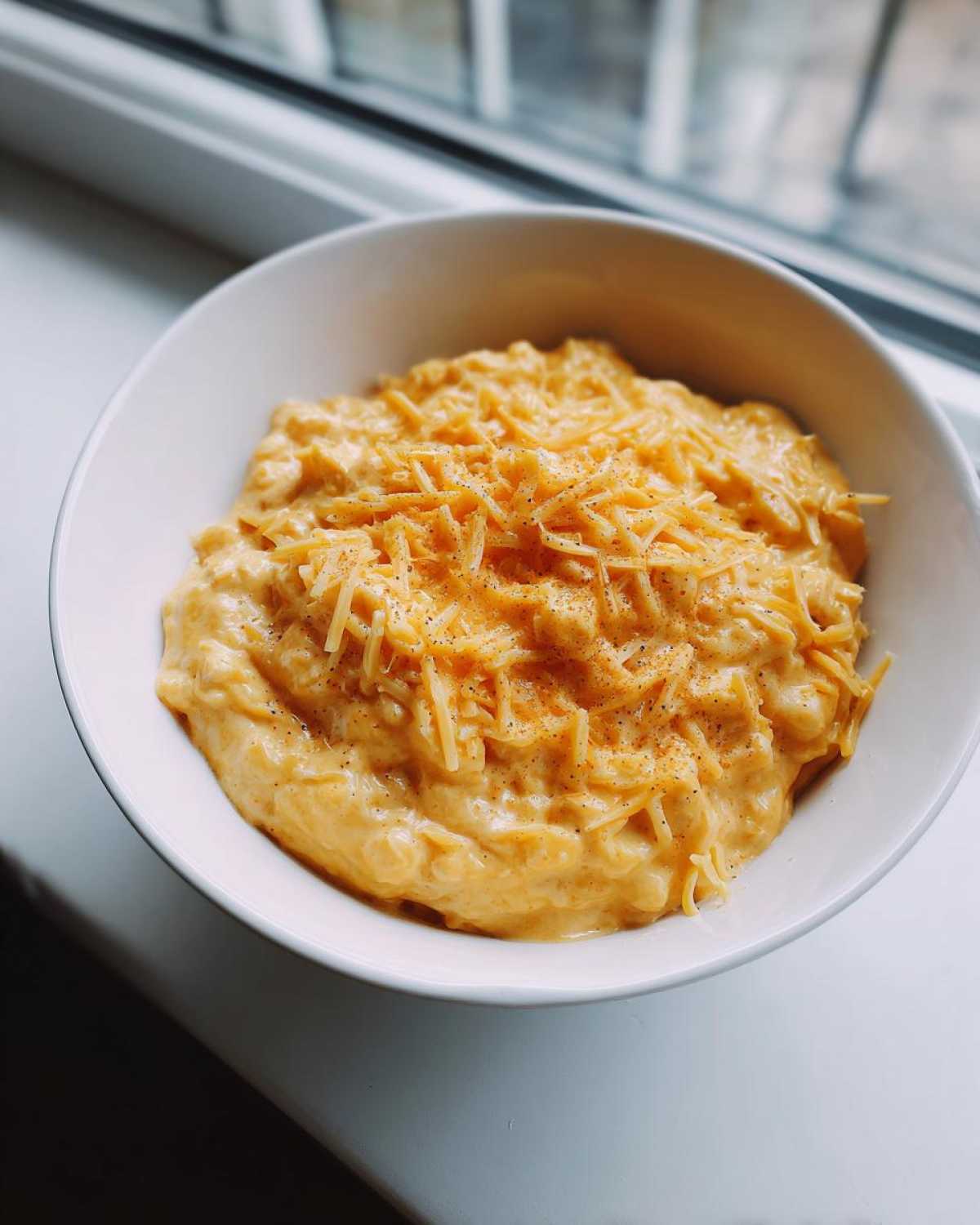 A white bowl filled with creamy, orange beer cheese dip, topped with shredded cheddar and black pepper.