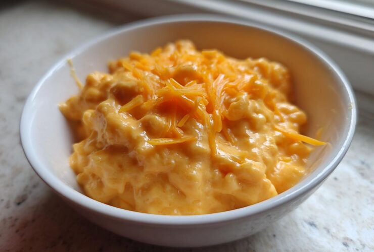 A small white bowl filled with thick, creamy, orange beer cheese dip, topped with shredded cheddar cheese.