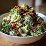 Close-up of a bowl filled with creamy broccoli salad featuring bacon, raisins, and sunflower seeds.