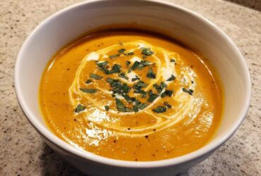 A close-up of creamy, vibrant orange butternut squash soup topped with a swirl of cream and fresh herbs.