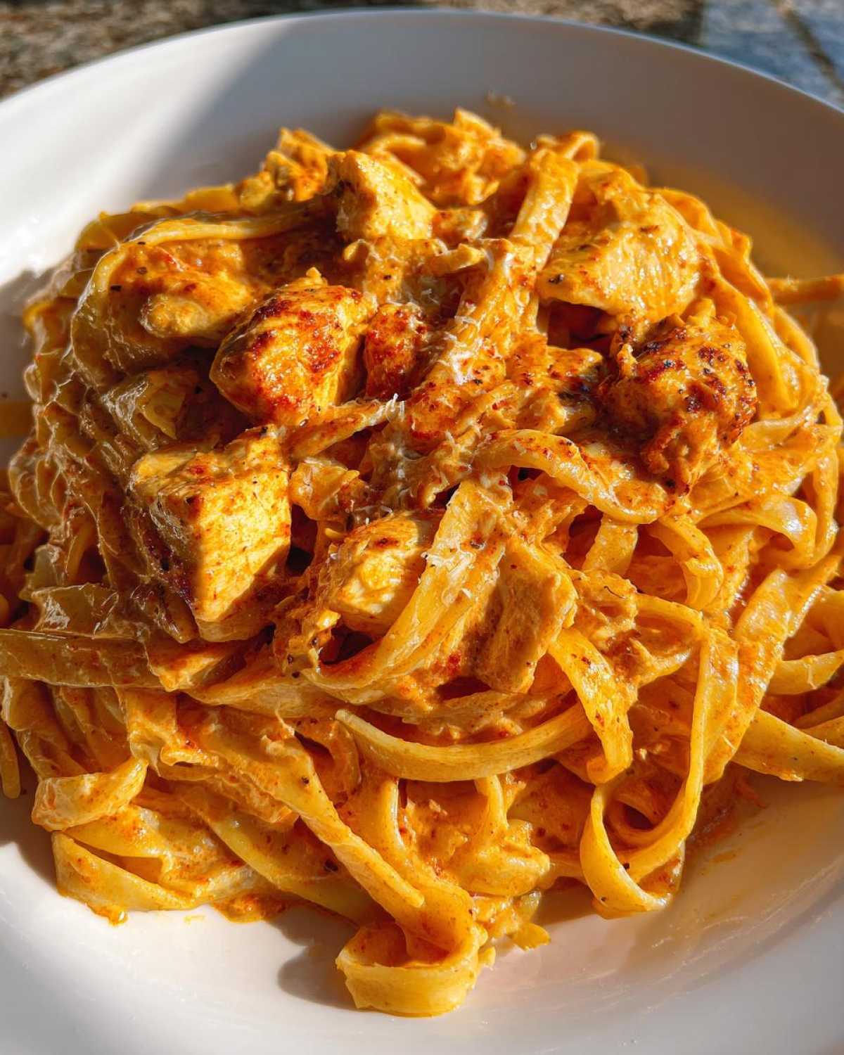 Close-up of creamy cajun chicken pasta featuring fettuccine noodles coated in an orange, spicy sauce with chunks of seasoned chicken.