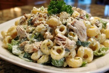 Close-up of creamy chicken caesar pasta salad featuring elbow macaroni, shredded chicken, and romaine lettuce, topped with Parmesan and parsley.