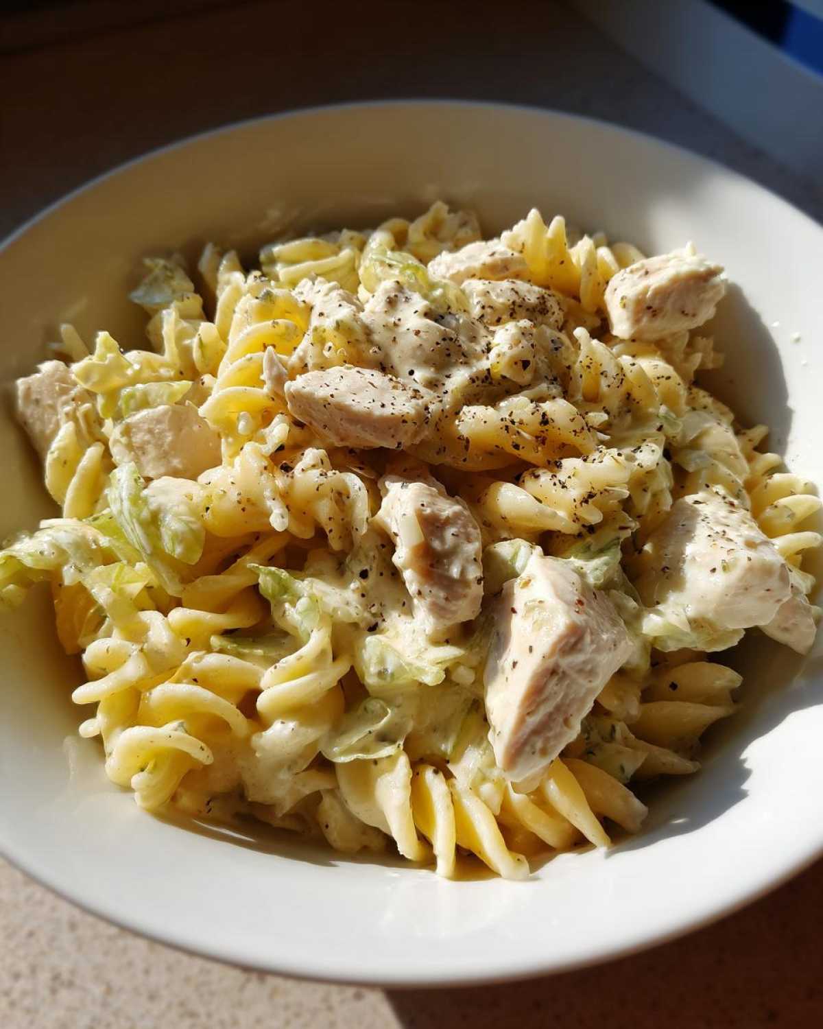 Close-up of creamy chicken caesar pasta salad with rotini pasta, chicken chunks, and black pepper.