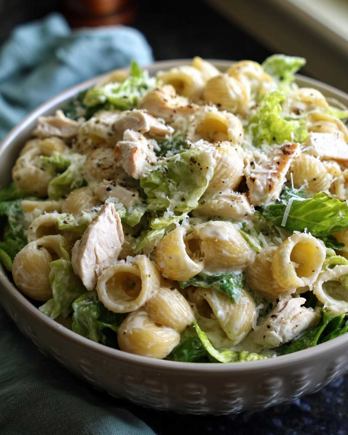 Close-up of creamy chicken caesar pasta salad featuring shell pasta, chopped chicken, and romaine lettuce.