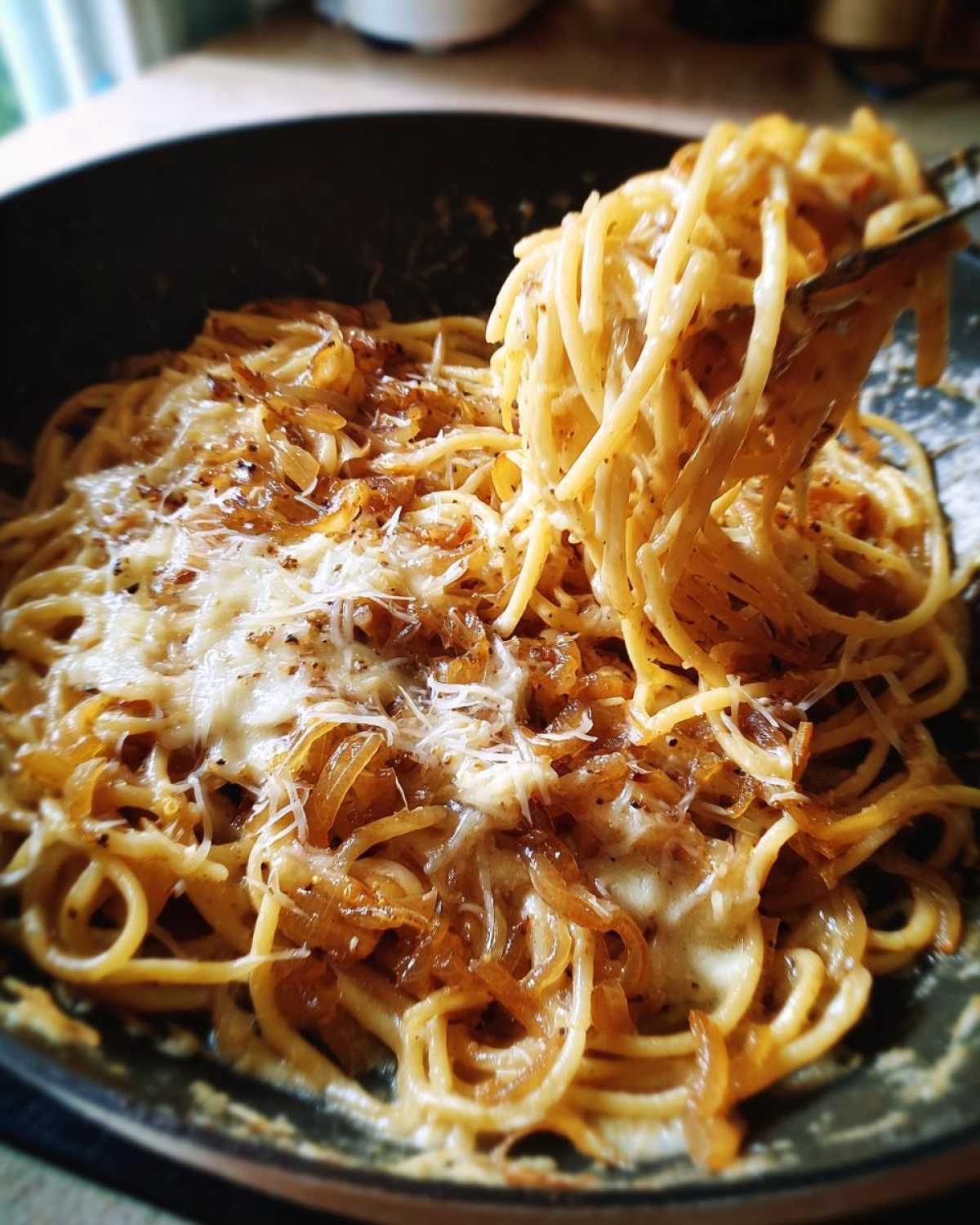 Close-up of creamy french onion pasta topped with melted cheese and caramelized onions, with a fork lifting a portion.
