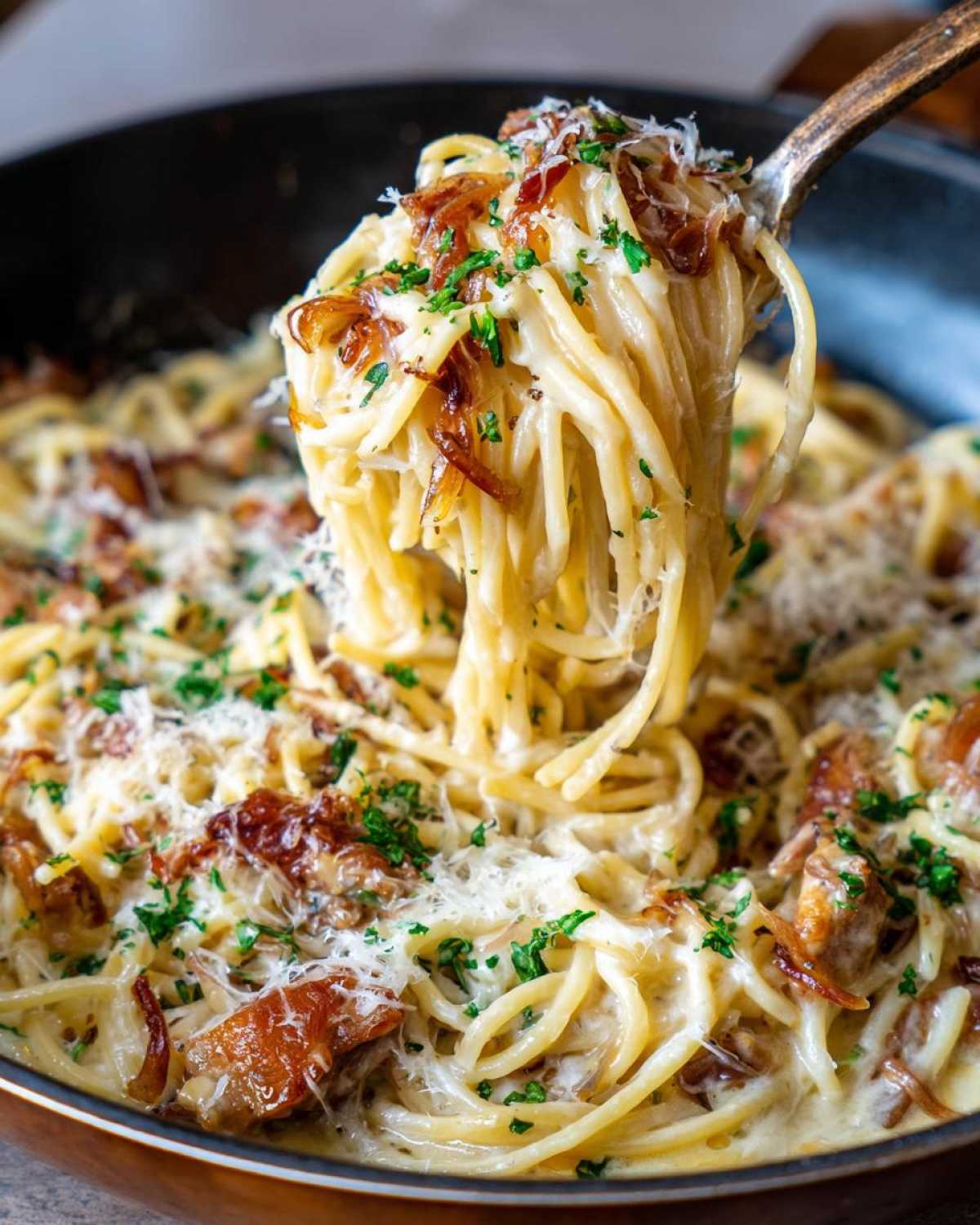A fork lifts a generous portion of creamy french onion pasta topped with caramelized onions and parmesan cheese.