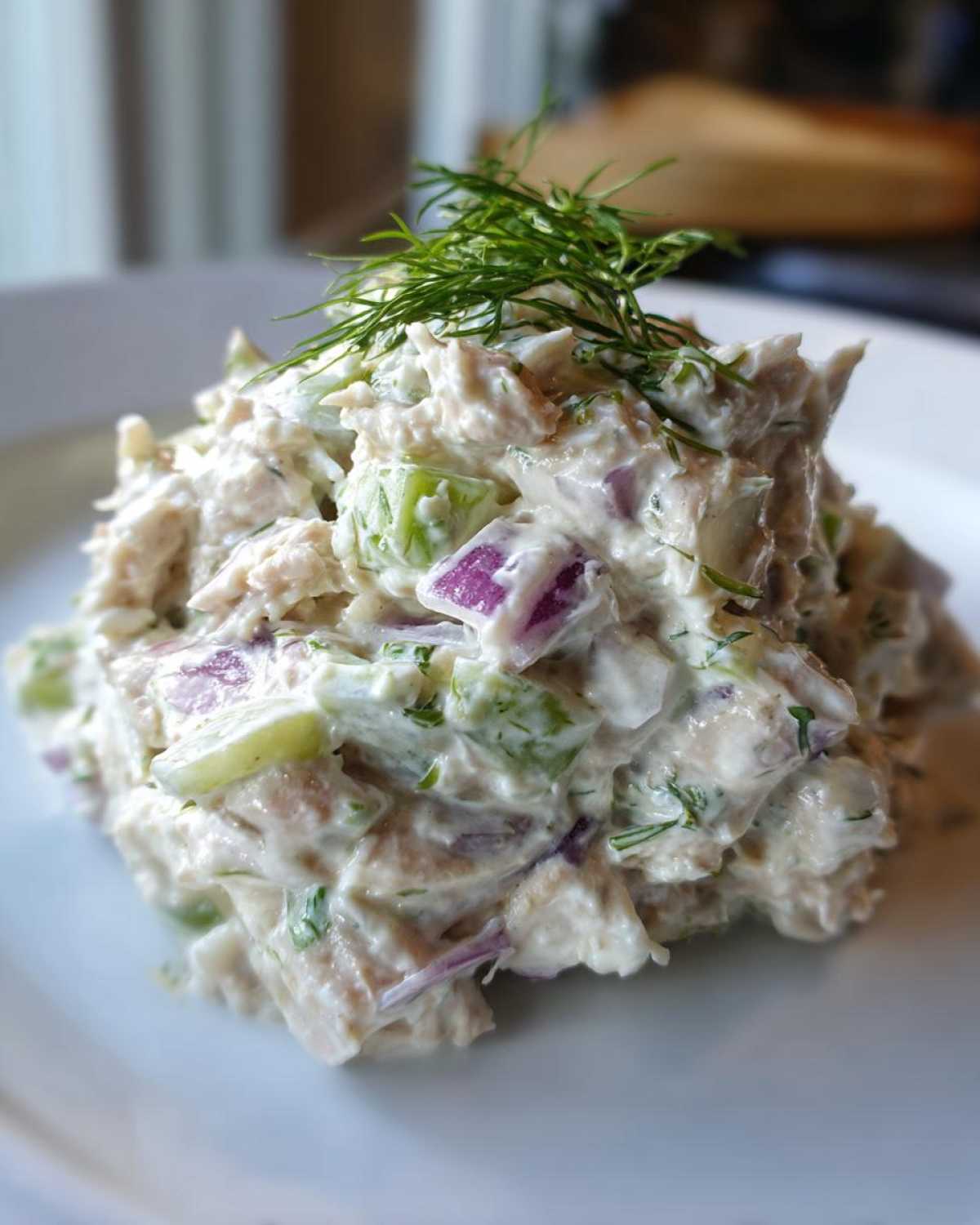 A mound of creamy healthy tuna salad mixed with visible chunks of red onion and celery, topped with fresh dill.