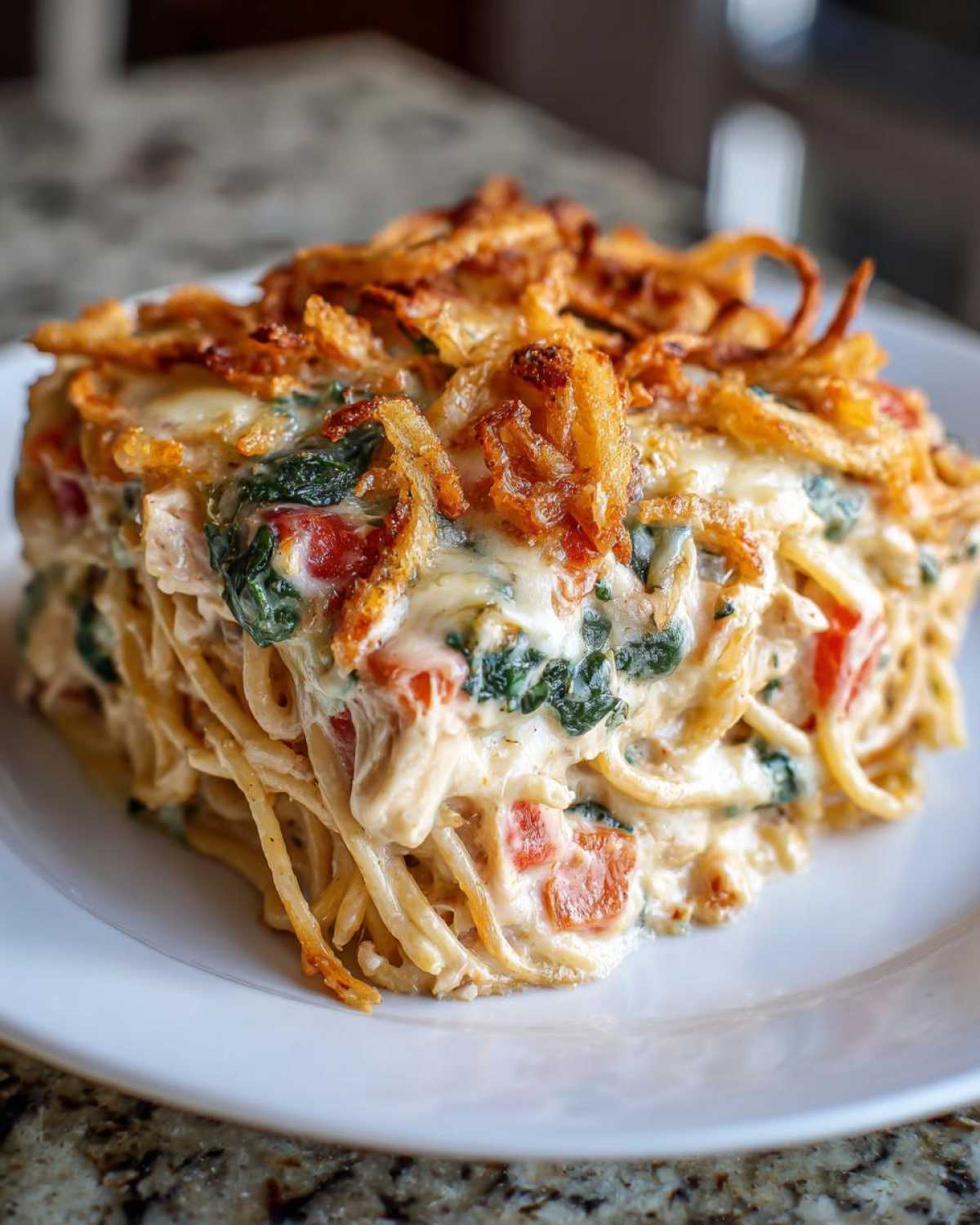 A square serving of creamy monterey chicken spaghetti baked with spinach, tomatoes, and topped with crispy fried onions.